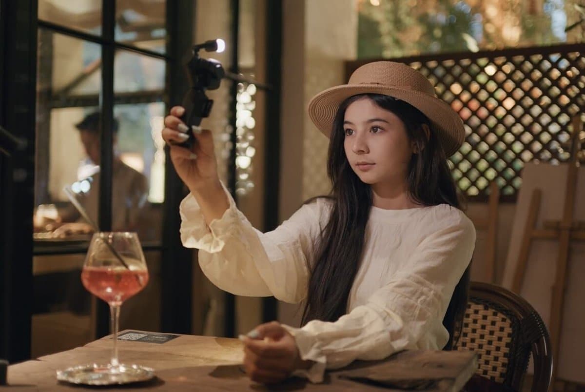 Cô gái dùng DJI Osmo Pocket 4P quay trong quán cà phê ánh sáng vàng buổi tối